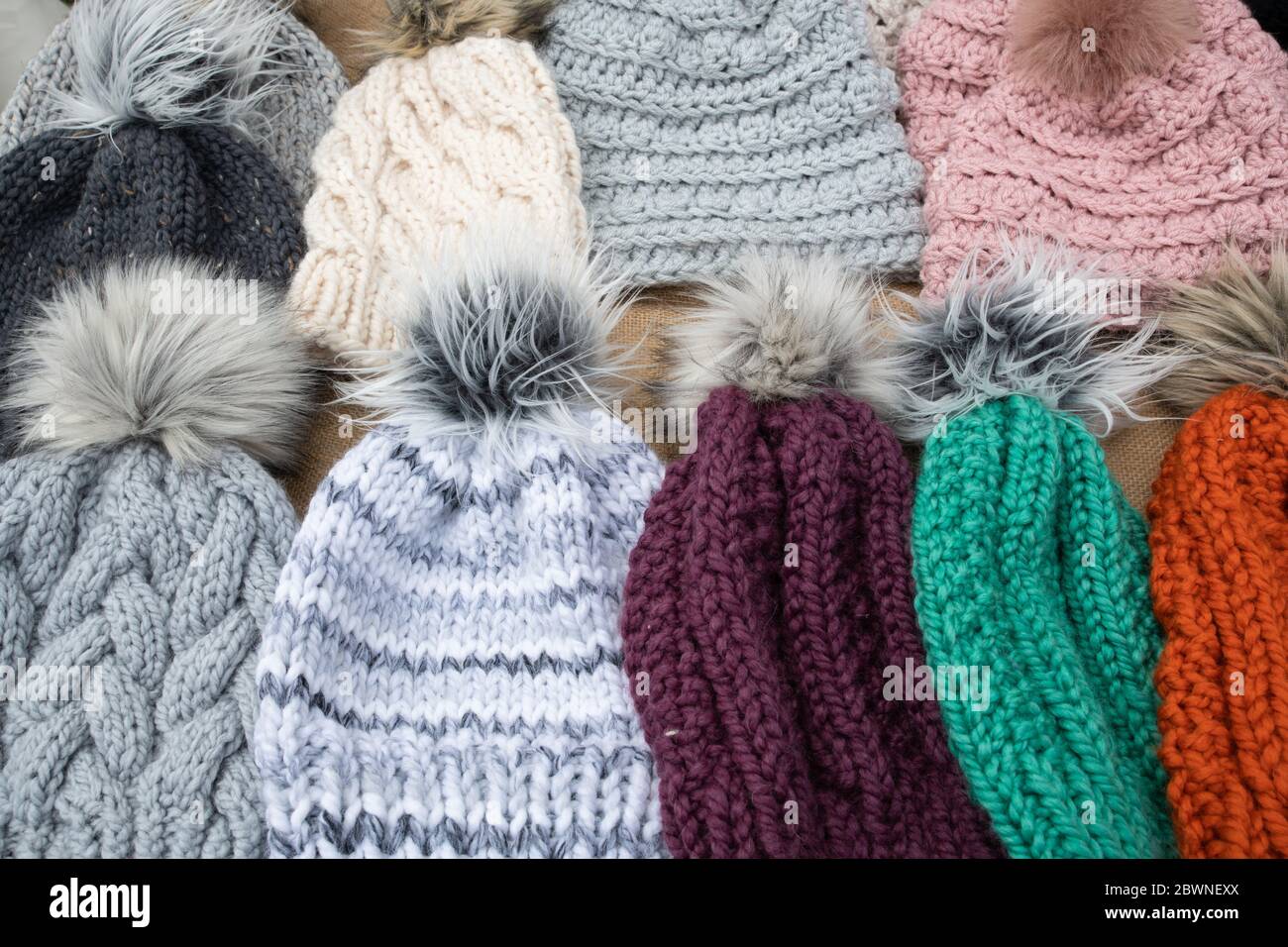 selection of hand crafted hats by knit or crochet with fake fur pom poms on a table for sale at a craft fair Stock Photo