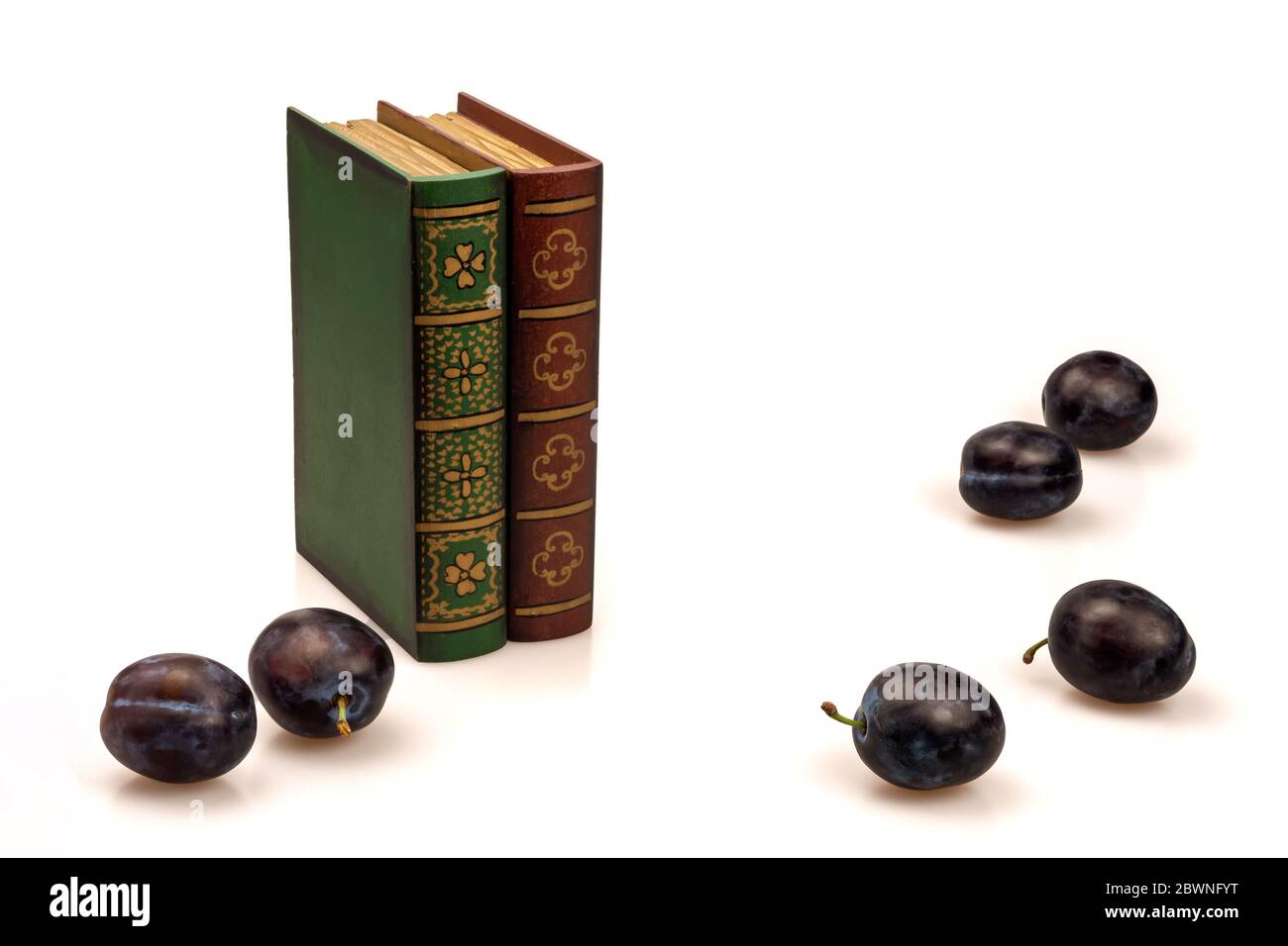 Books and ripe purple plums on a white background. Stock Photo