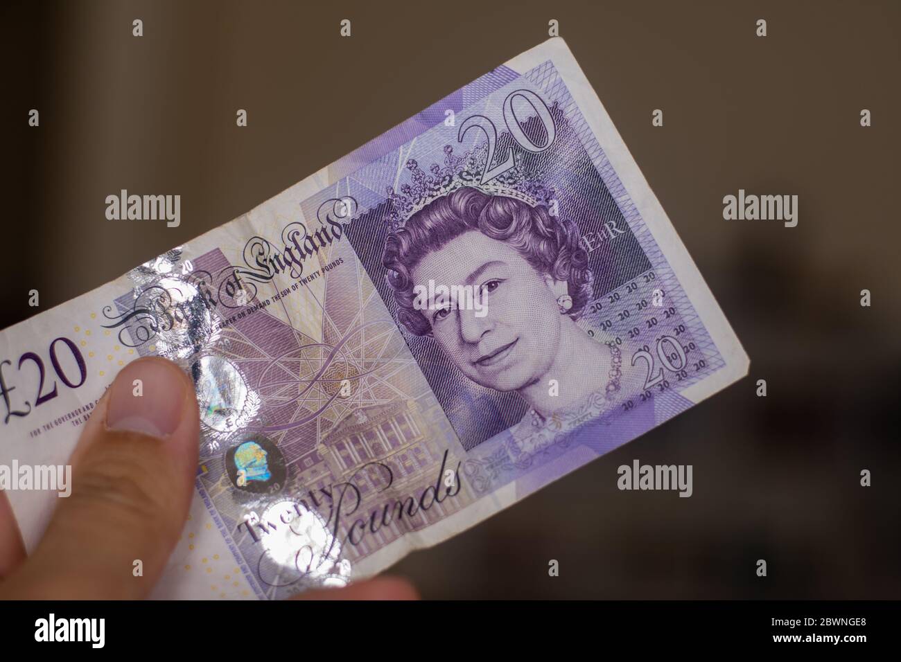 Persons hand giving the Currency of the England in the United Kingdom - One purple twenty pound note spread out on a brown background. Money exchange. Stock Photo
