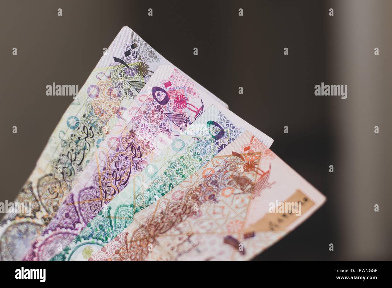 Persons hand giving the Currency of the Qatar - hundreds of rial or riyal notes spread out on a brown background. Money exchange. Stock Photo