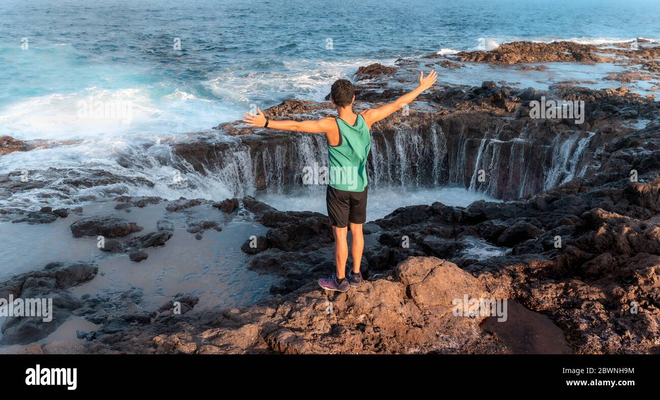 panoramic photo. young man is standing in front of a rock formation and raises his arms in admiration to see how the water disappears into the hole Stock Photo