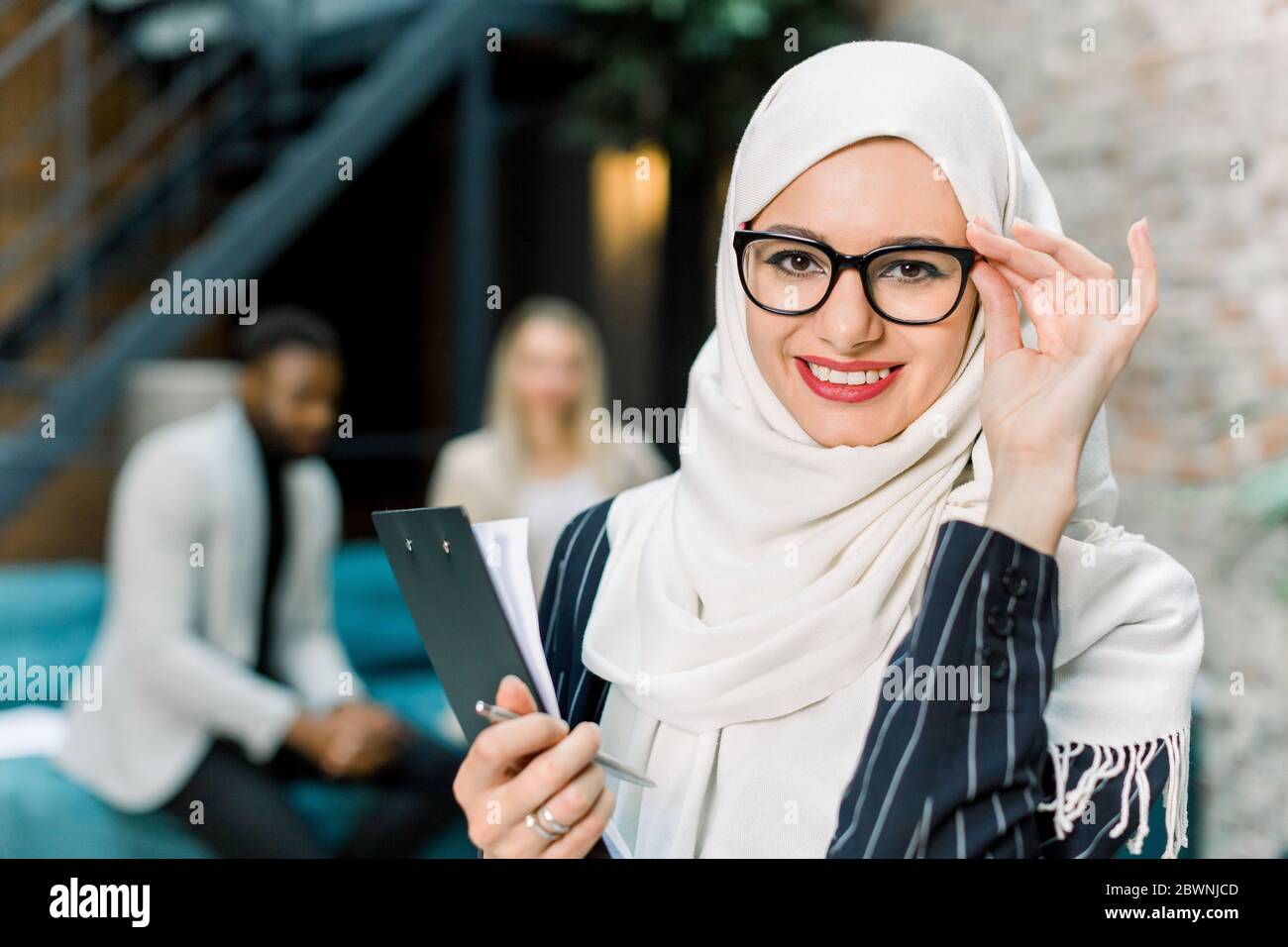 Charming arabian Muslim business woman in white hijab holding folder of ...