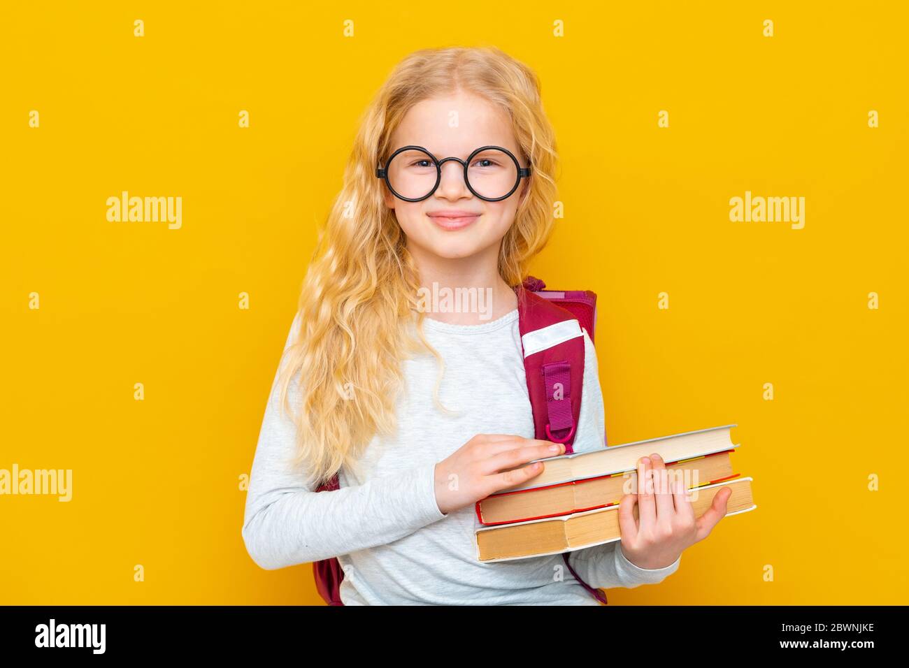 Back to school. Portrait of blonde school girl in round glasses with bag and books. Yellow studio background. Education. smiling at camera. Stock Photo
