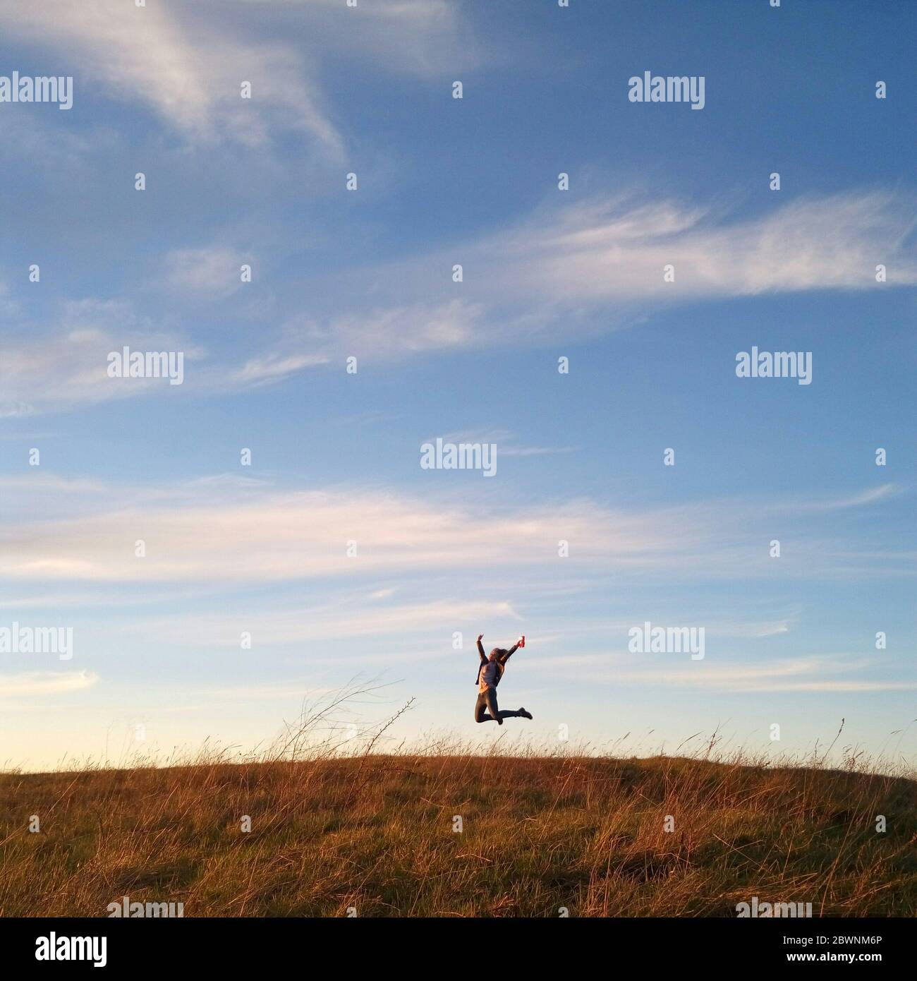 Happy girl is jumping on field outdoor scene over the beautiful evening sky with clouds. Joy and happiness in human life. Achieving success, striving Stock Photo