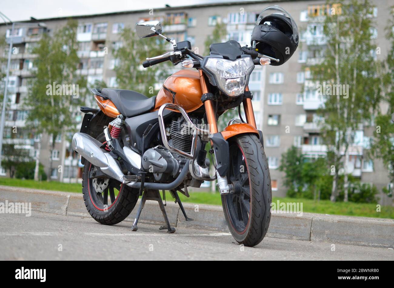 Orange motorcycle with black helmet parked on a summer day. Stock Photo