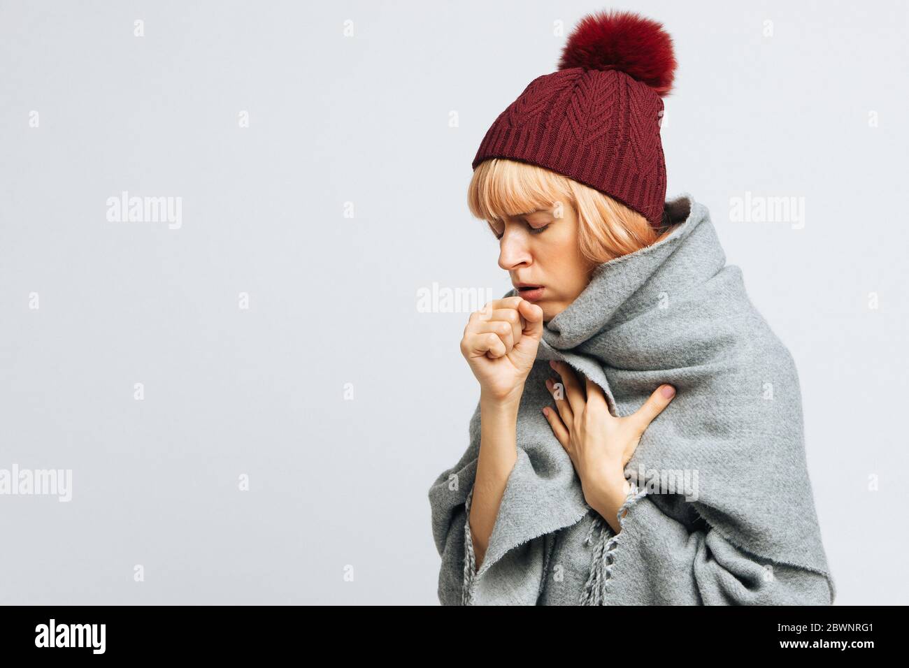 woman in red hat, wrapped in warm scarf coughing, closed eyes.Female