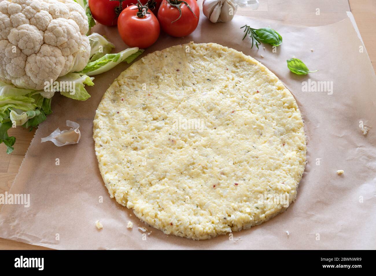 Vegetable pizza base from shredded cauliflower and cheese on baking paper, healthy alternative for low carb and ketogenic diet,  view from above, sele Stock Photo
