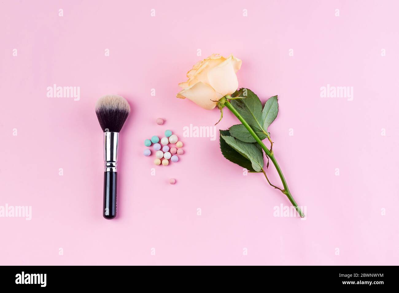 Set of colorful cosmetics powder balls and brushe with rose on pink background. Makeup Accessories Top view Flat Lay Stock Photo