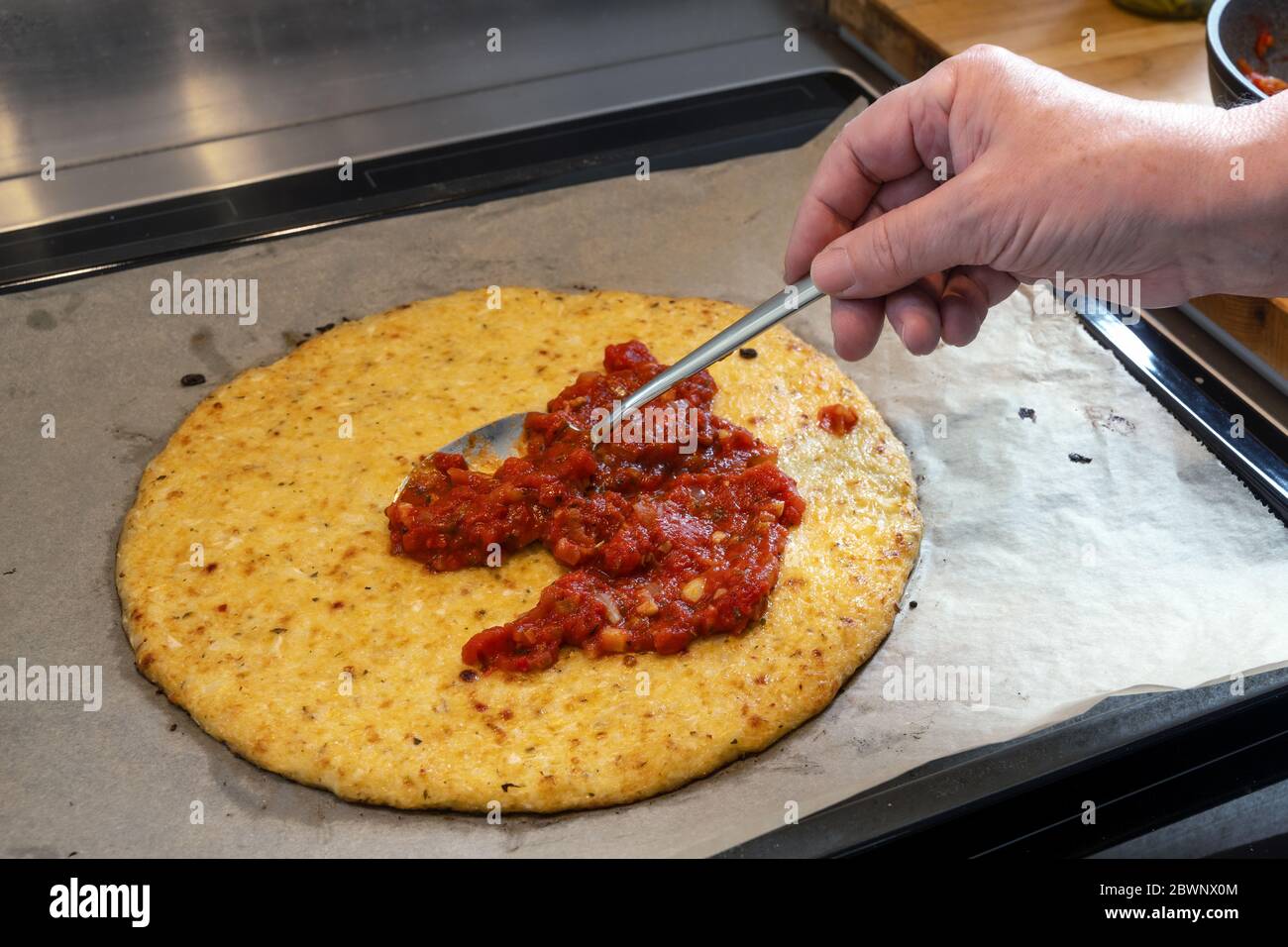 Hand is spreading tomato sauce on a pizza crust from shredded cauliflower, cooking a healthy alternative for slimming with low carb or ketogenic diet, Stock Photo