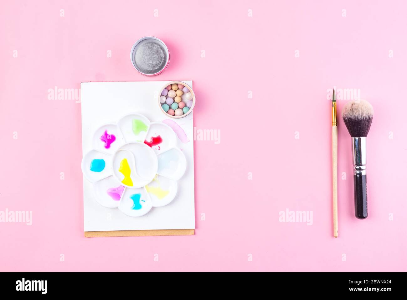 Set of colorful cosmetics powder balls, paper with watercolor stick and brushe on pink background. Makeup as art Stock Photo