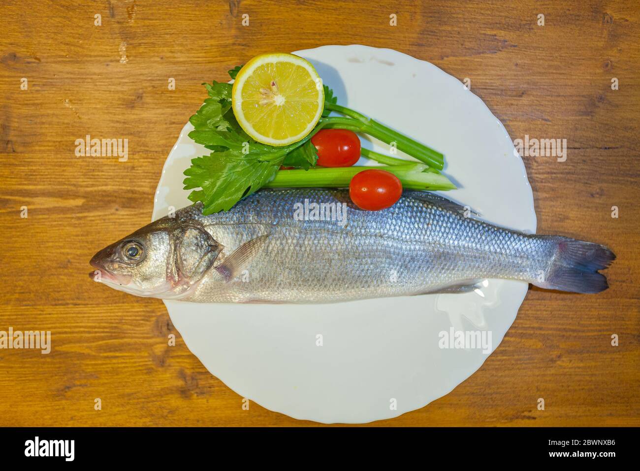 Dish with sea bass, lemon, celery and tomatoes on wooden background Stock Photo