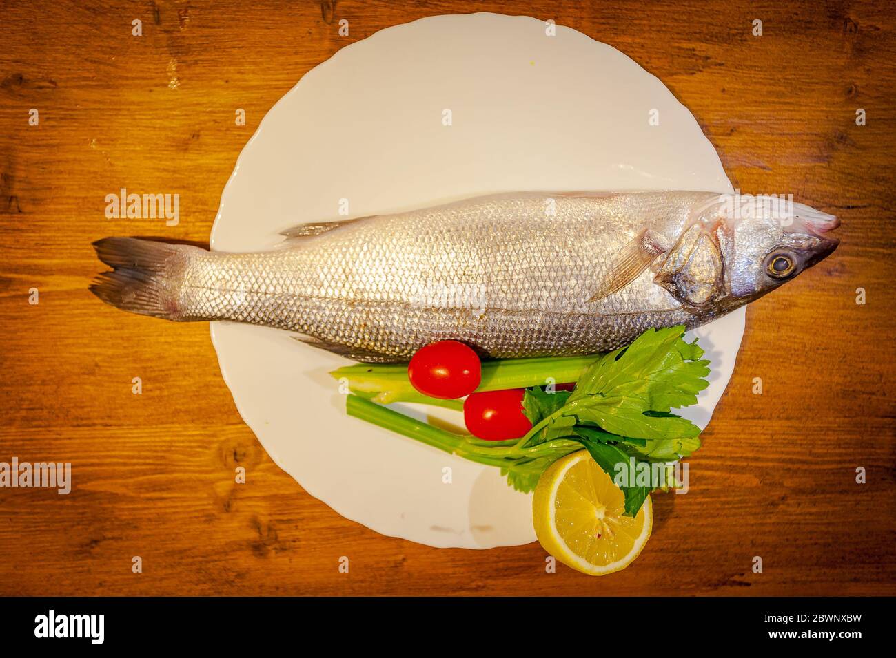 Sea bass, lemon, celery and tomatoes on wooden background Stock Photo