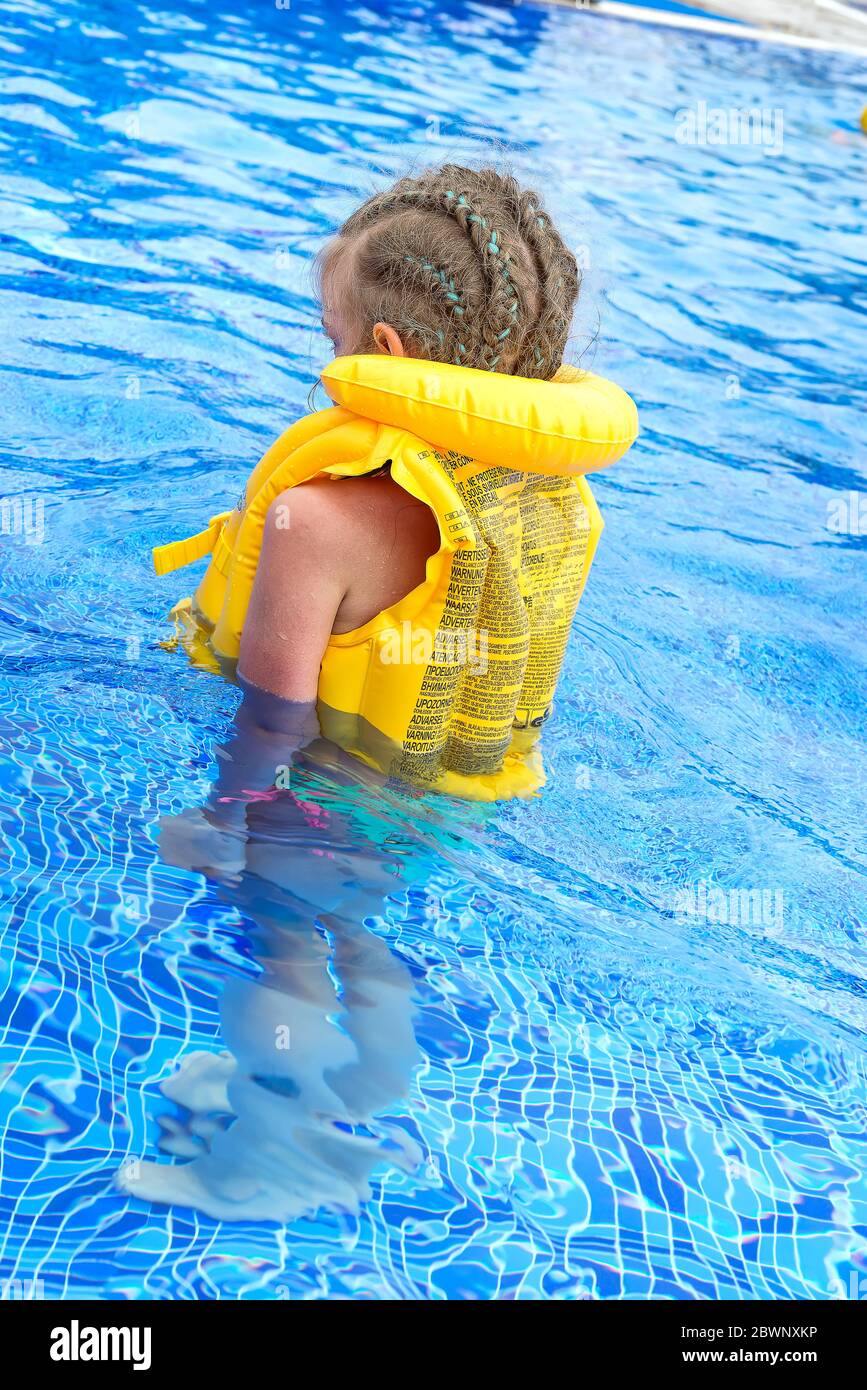 Child learning to swim in Life jackets in blue swimming pool. Summer