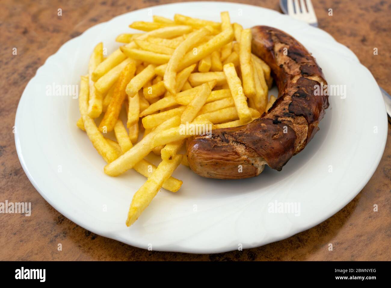 Grilled sausage, German Bratwurst, and french fries on a plate in a fast food restaurant, tasty but unhealthy eating with trans fat and saturated fatt Stock Photo
