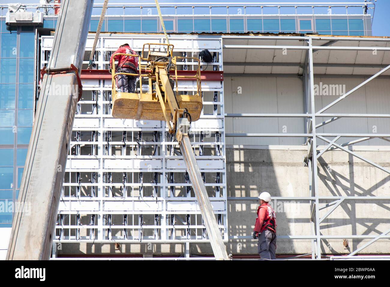 Belgrade, Serbia - May 6, 2020: Construction workers in crane basket installing external cladding metal structure on a building facade wall Stock Photo