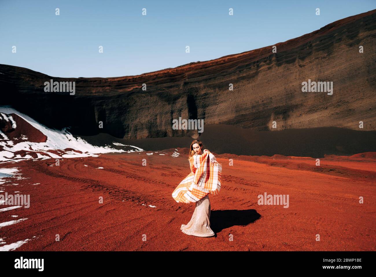 The girl waves a blanket. Portrait of a bride model in a golden wedding evening dress, in a yellow-red sandy quarry, in the crater of a volcano in Stock Photo