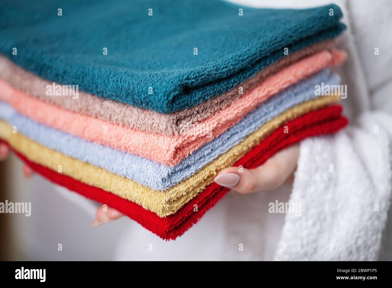 Woman in a white coat holding a stack of colored towels Stock Photo - Alamy