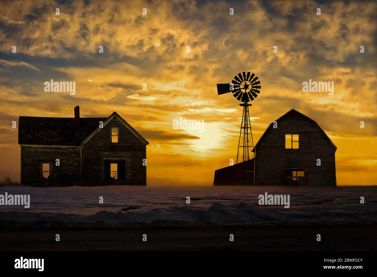 horizontal image of a an old abandoned farm house and barn looking desolate with a beautiful ornage sunset looming in the background on a cold winter Stock Photo