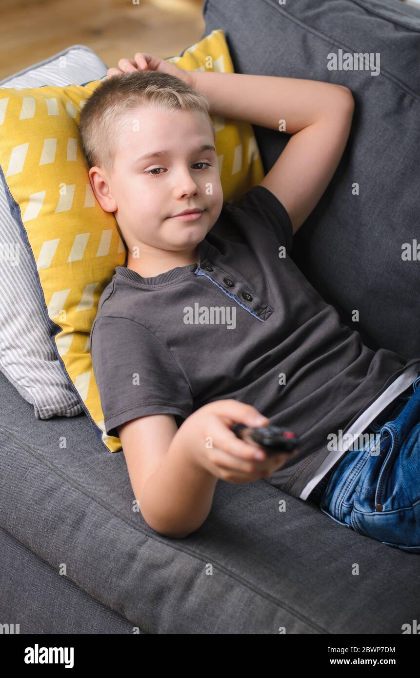 Teenage boy laying on sofa watching tv at home. Boy switches remote