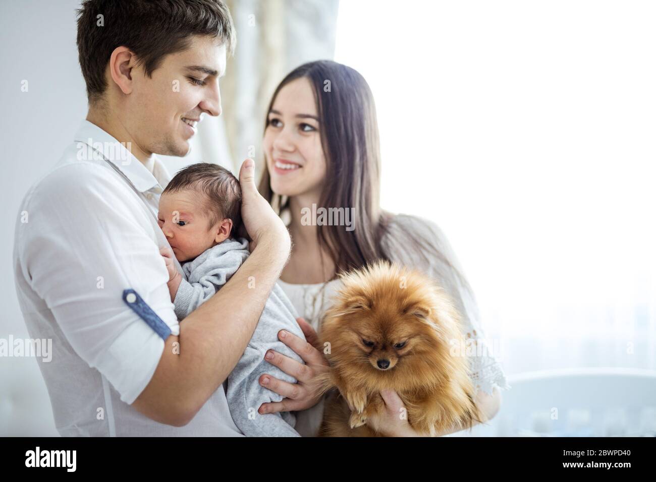 Happy young couple and their newborn baby boy. Beautiful young mom holding lap-dog. Stock Photo