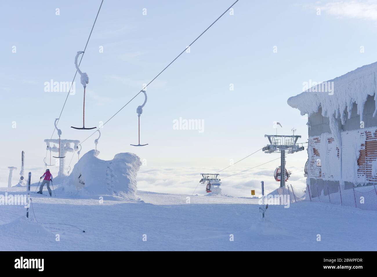 a single skier heads down a run having disembarked from ski lifts that rise up above the clouds into the pale blue sky. Very cold and snowy conditions Stock Photo