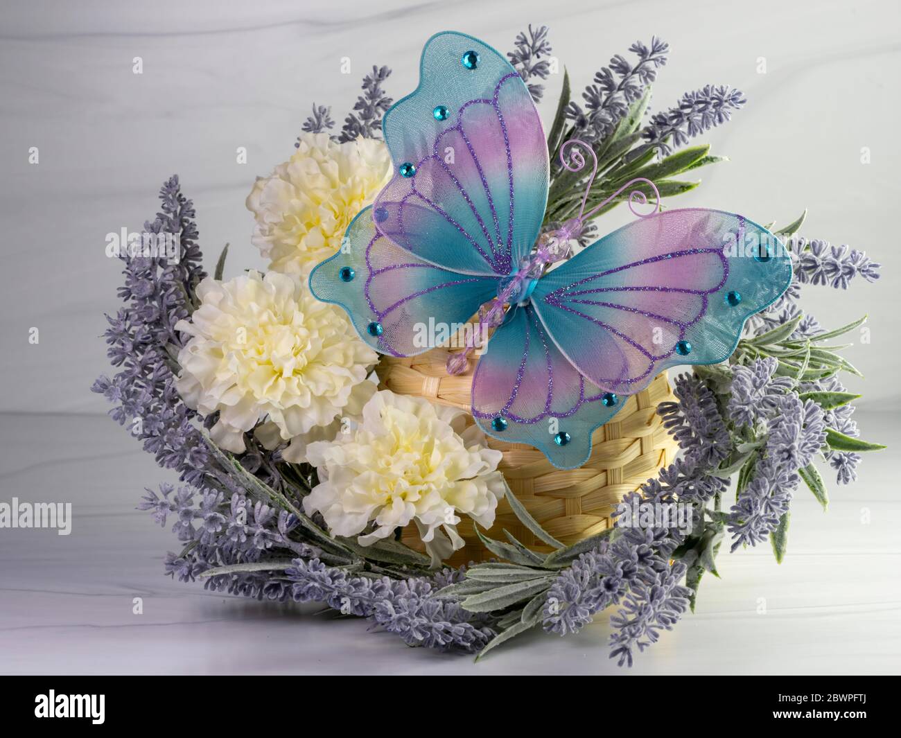 Lavender wreath with white carnations and a mesh blue and purple butterfly decorated with blue gem stones.  Purple flowers and white flowers on a neut Stock Photo