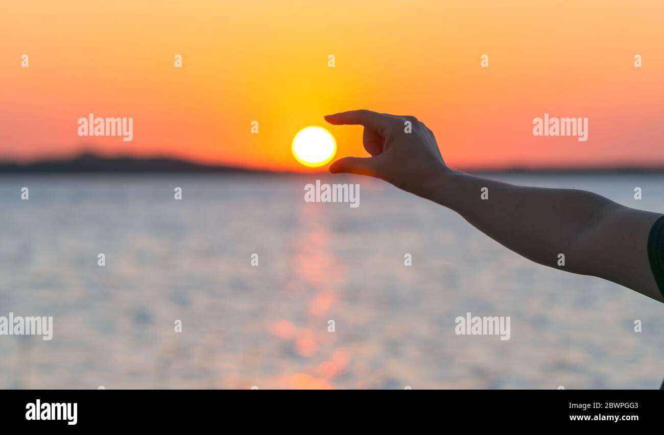 Silhouette woman hand catch holding the sun in fingers at sunset on the ...