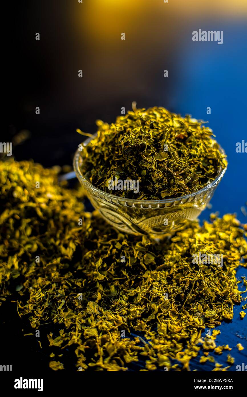 Close up short of popular Indian Spice Kasuri Methi (Dried Fenugreek Leaves) in a bowl and some on a spoon on a black colored glossy surface. Stock Photo