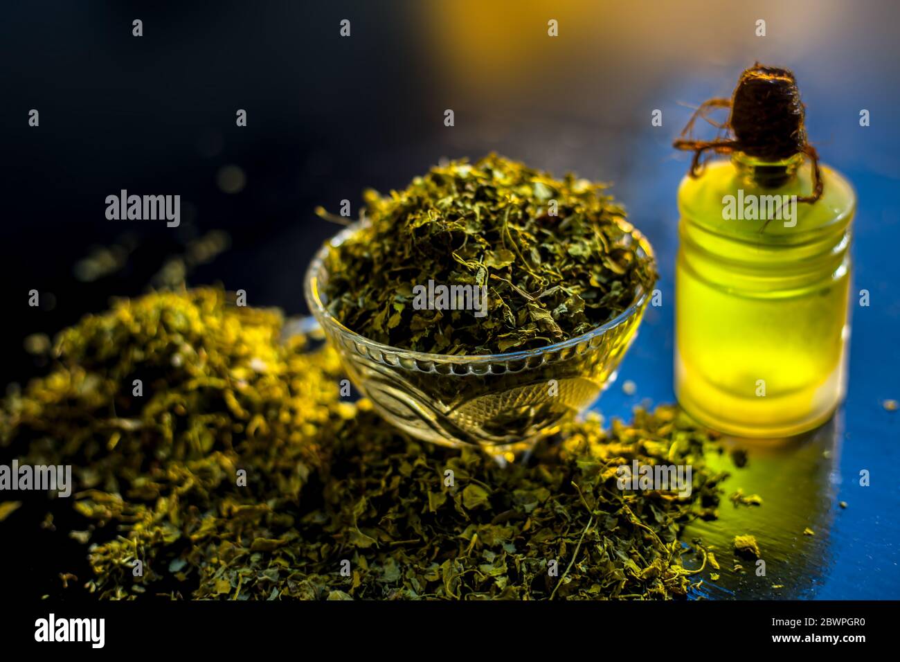 Shot of essential oil of Kasuri Methi or Dried Fenugreek in a glass bottle along with some dried powder fenugreek in a bowl. Stock Photo