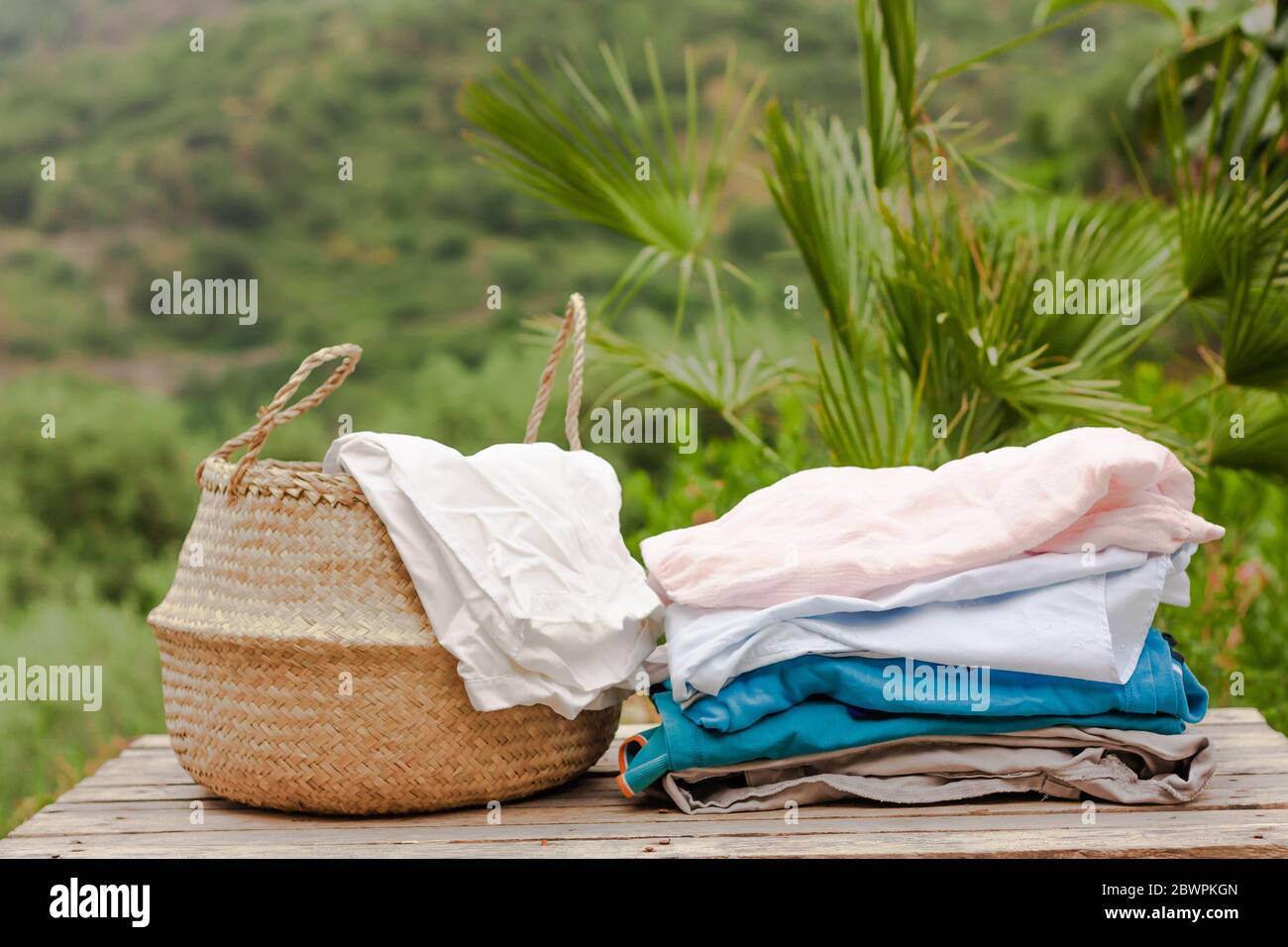 Basket with clean and dry laundry on wooden table on nature background in sunny day Stock Photo