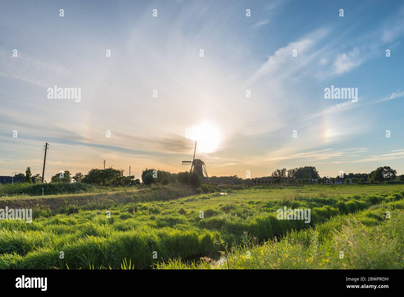 Circular halo with sundogs (parhelia) to the left and right of the sun over a windmill in a classic dutch landscape Stock Photo