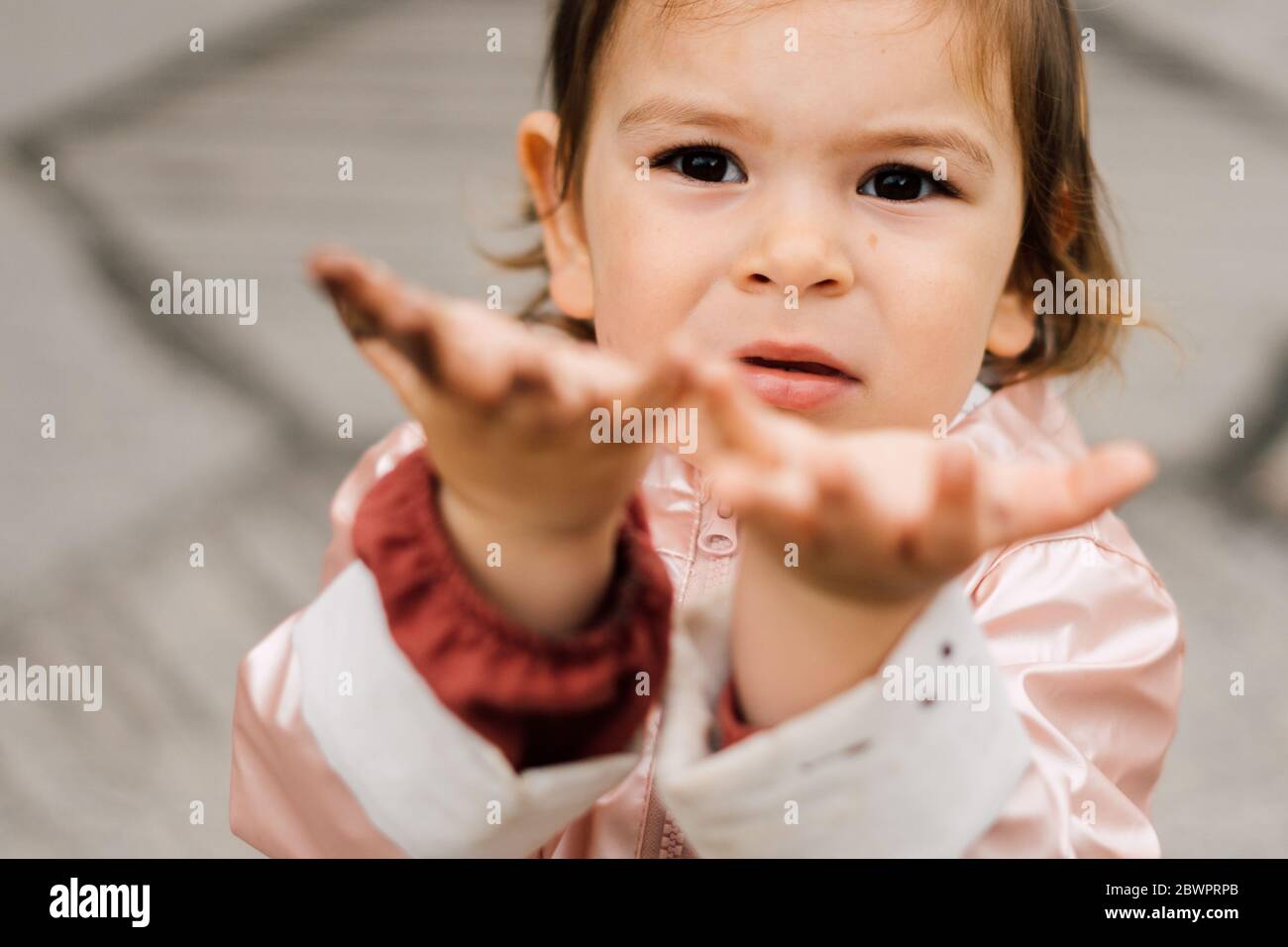Pink raincoat dirty in mud. Hands of the child. Spring autumn outdoors
