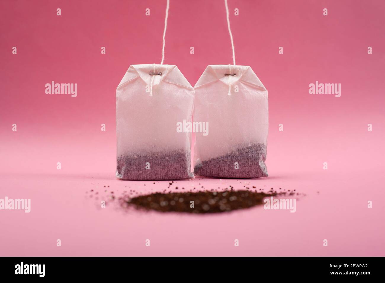 two paper bags with tea and with a bunch of black loose tea on a pink background close-up. Stock Photo