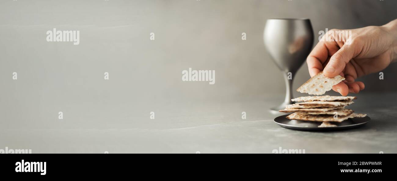 Hands with chalice and communion matzo bread, wooden cross on grey
