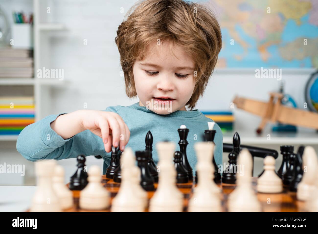 Kid Playing Chess. Kids educational games, child early development. Clever concentrated and thinking child while playing chess. Stock Photo