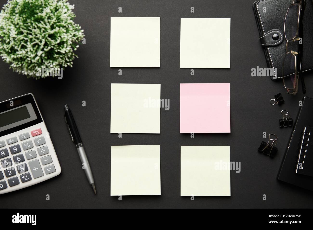 Top view of modern black office desk with calc, notebook, pen, blank sticker and a lot of things. Flat lay table layout. Copy space for text. Stock Photo