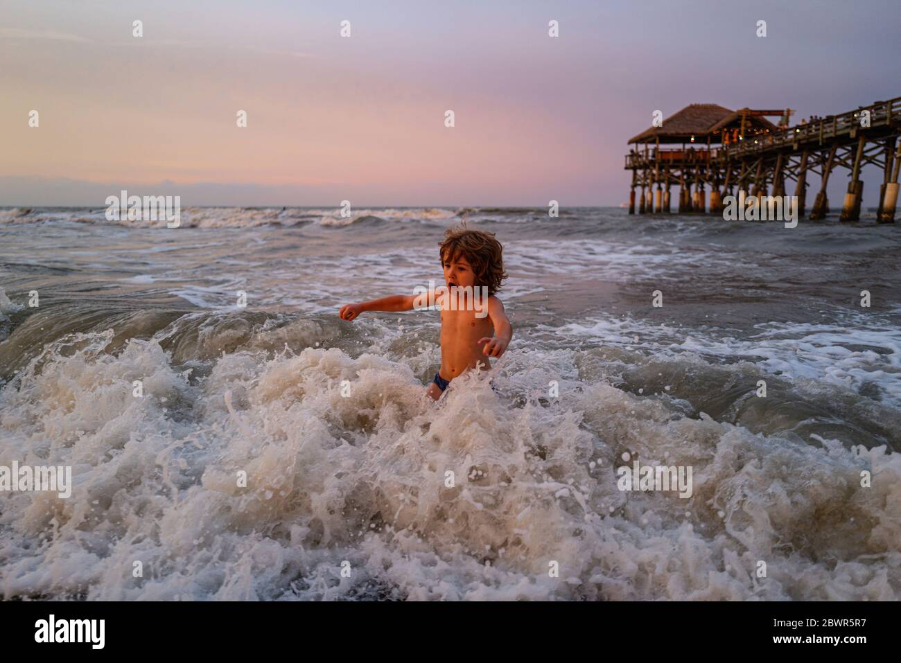 Kid jumping near the waves. Happy kid have fun in sea on beach. Travel lifestyle, swimming activities summer camp. Stock Photo