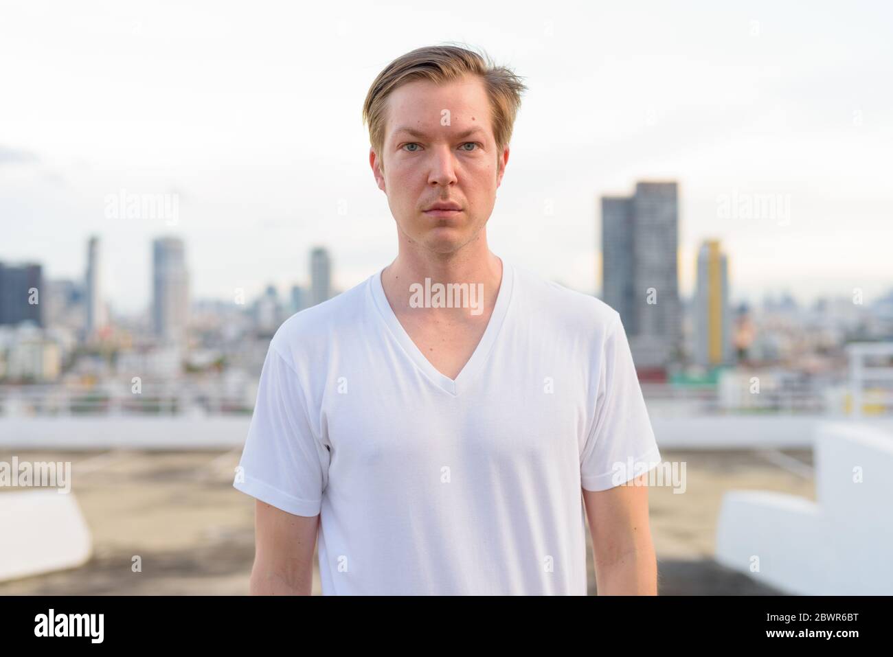 Portrait of young handsome man with blond hair against view of the city ...