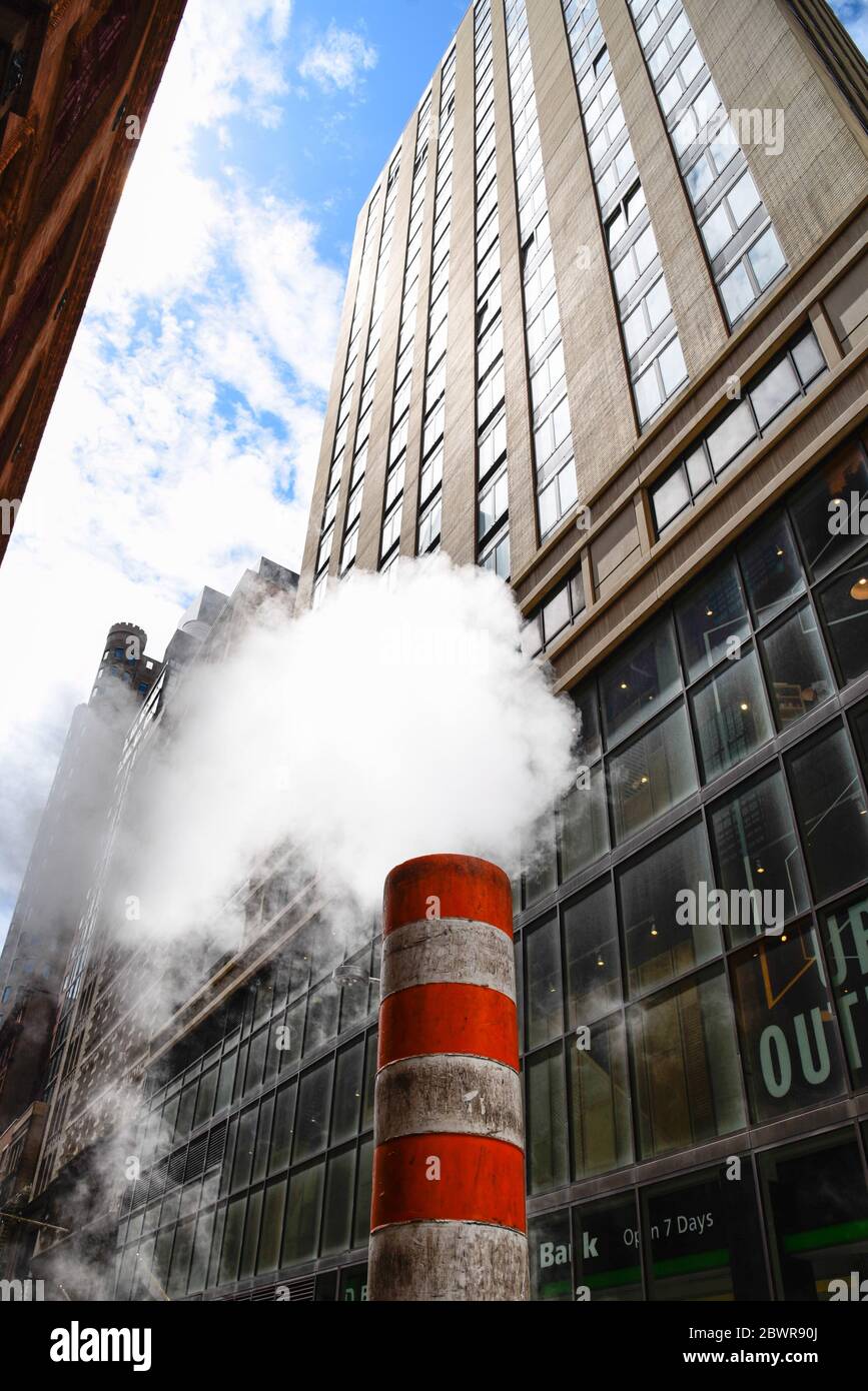 Low angle view of steam coming out stack for venting the district heating system in downtown of New York. Stock Photo