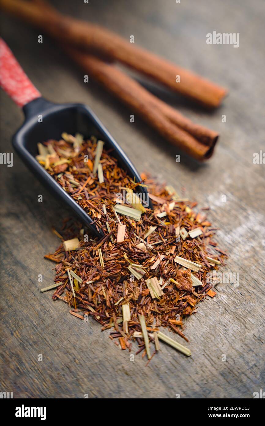 Close up of a handful of rooibos leaves placed on wooden surface with a japanese measuring tea spoon Stock Photo