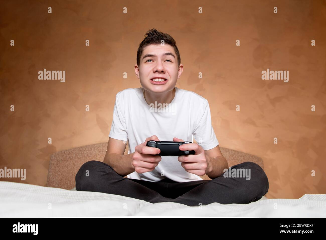 A boy in a white T-shirt enthusiastically plays a video game using a modified joystick without identification marks Stock Photo