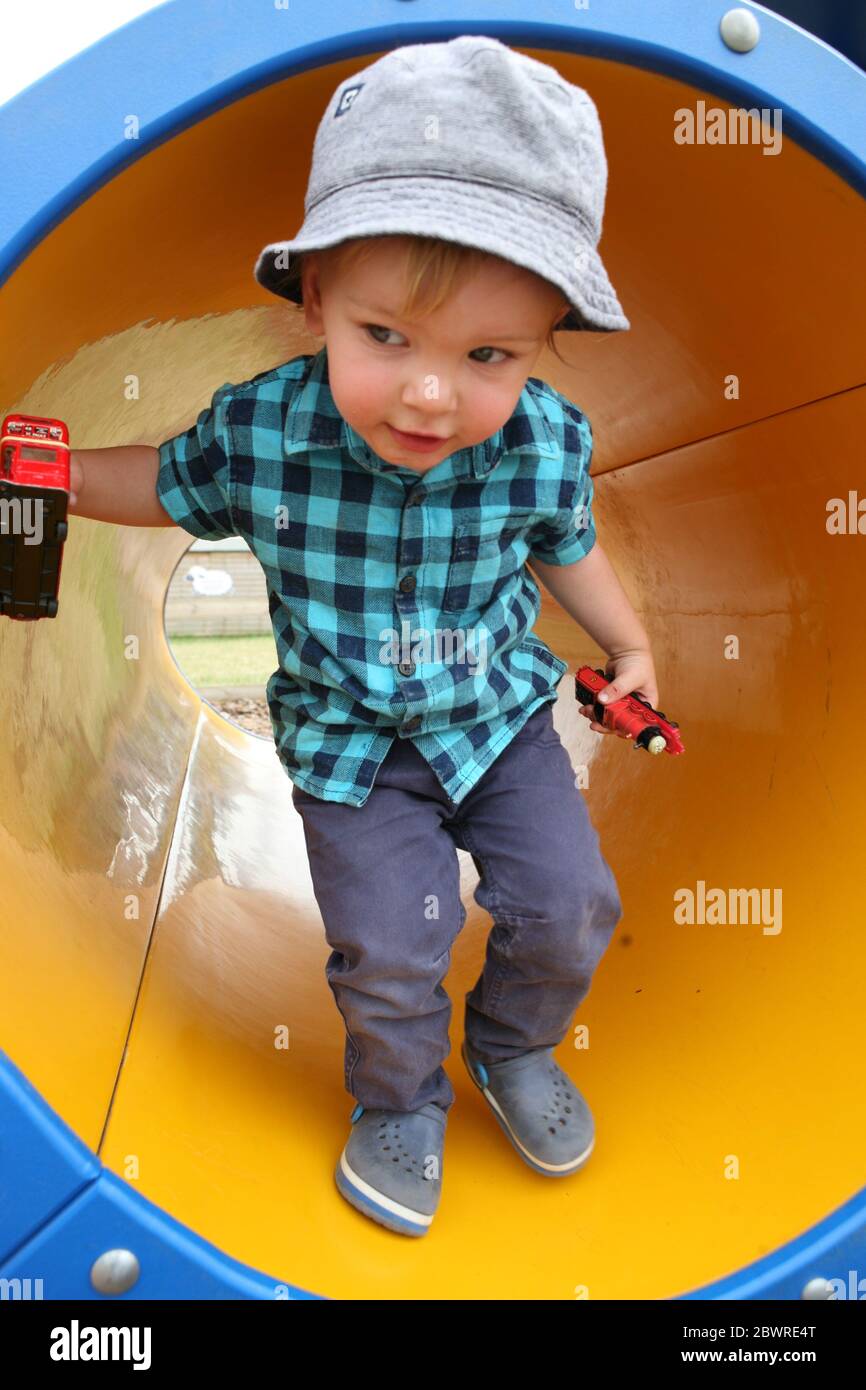 Little boy, two years old, happily playing in a tunnel in the playground at Manor Farm Country Park, Hampshire, England, UK.  MODEL RELEASED Stock Photo