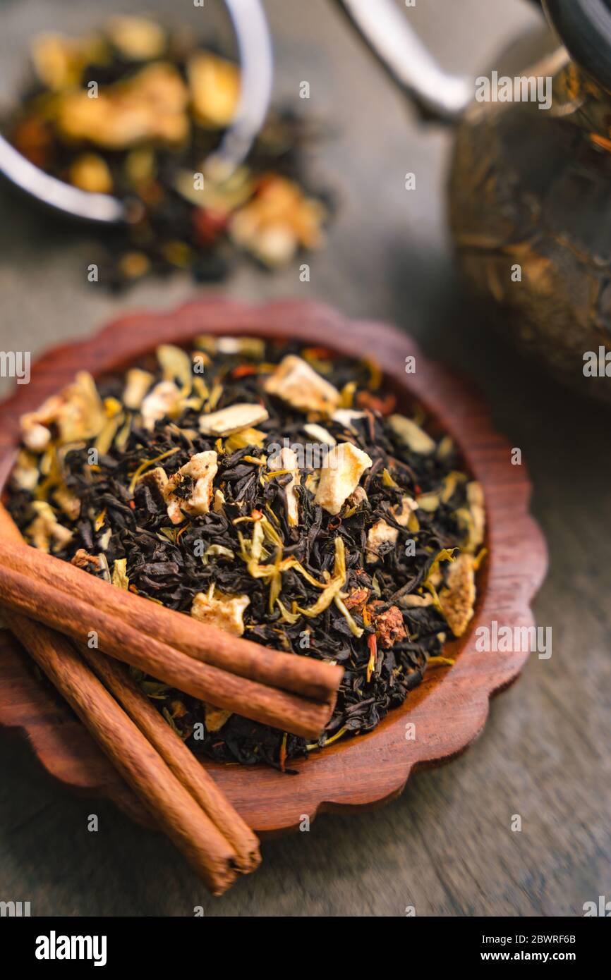 Close up of aromatic fruity black tea dry leaves on a small wooden tray, metal kettle and cinnamon bark strips Stock Photo