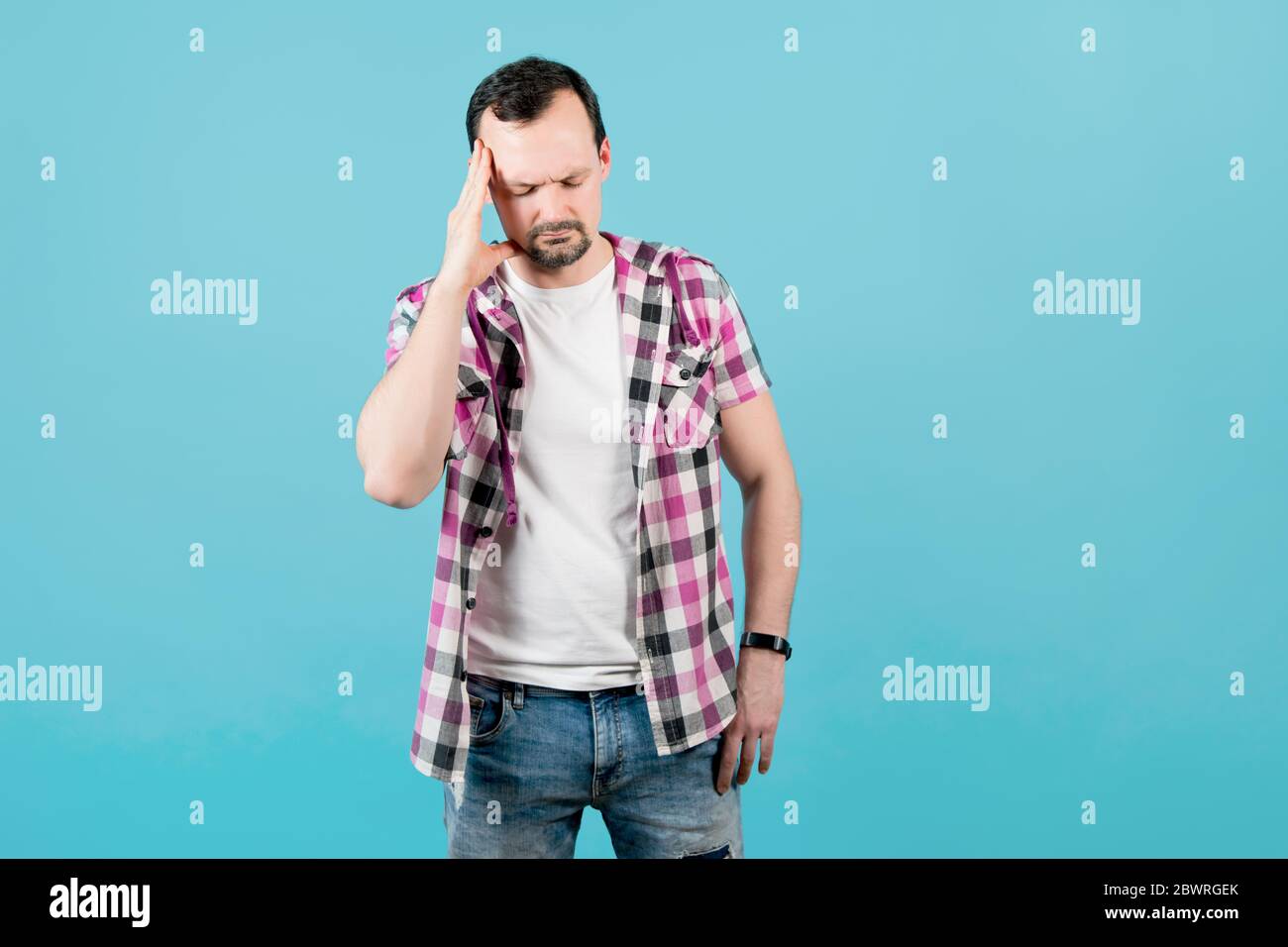 man with stubble in a plaid shirt holds his hand to his head, depicting pain Stock Photo