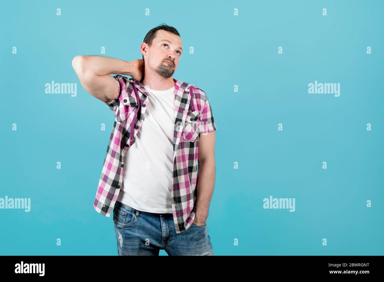 a man in a plaid shirt rubs his neck and looks up thoughtfully Stock Photo