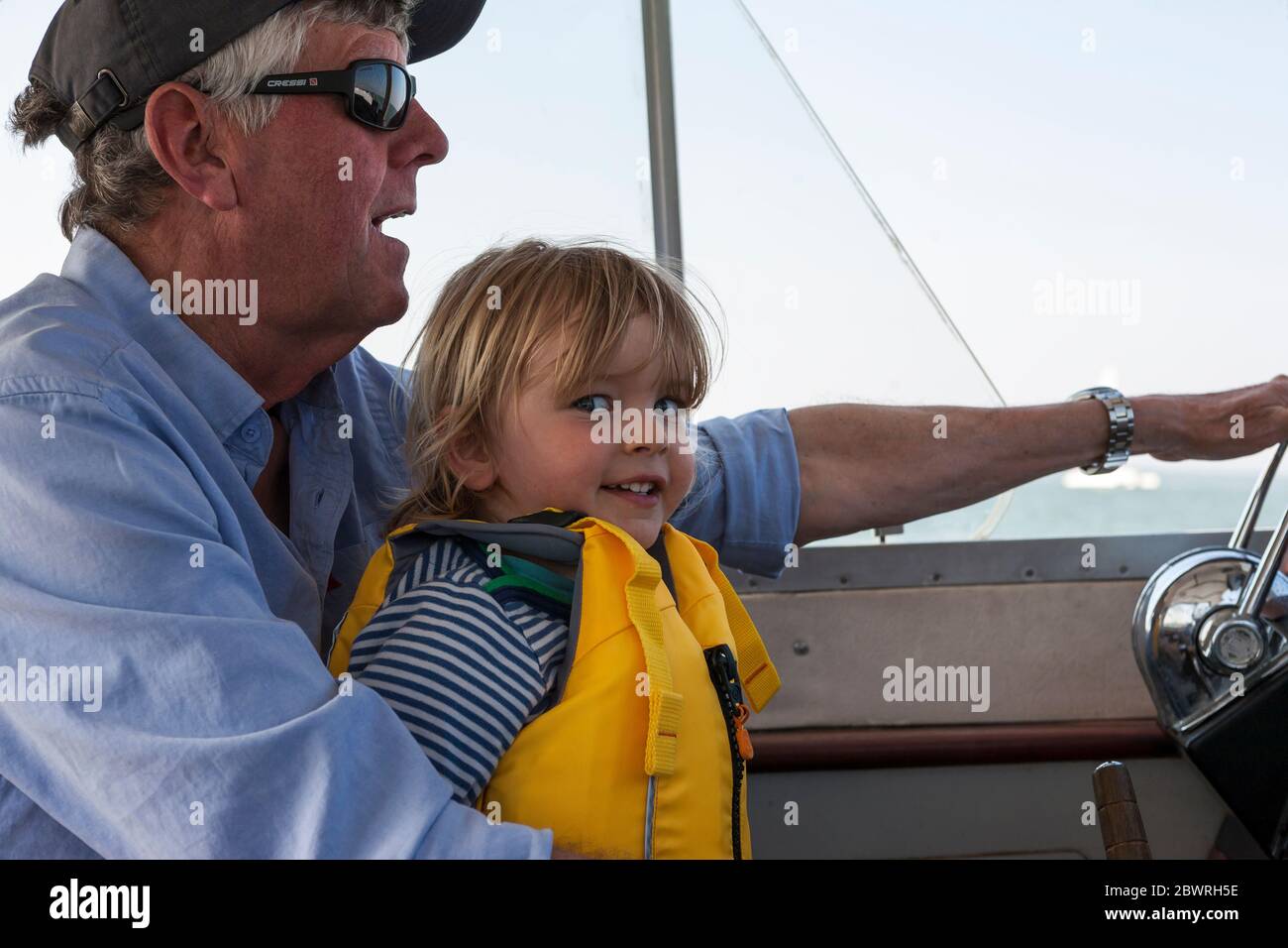 Small boy, 2-3 years old, excited to be helping his grandfather to steer his boat.  MODEL RELEASED Stock Photo