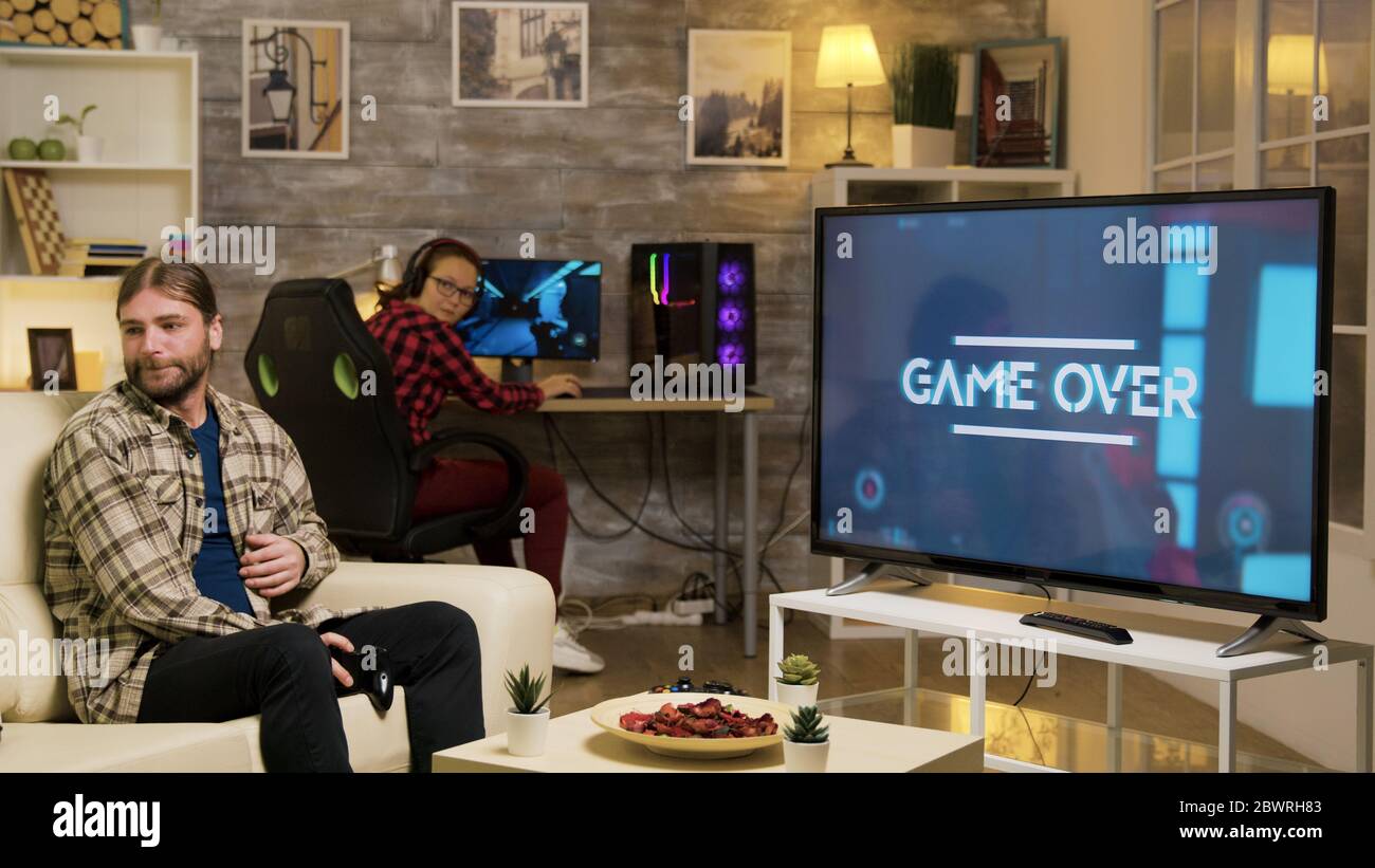 Game over for a young playing video games with vr headset sitting on sofa. Girlfriend looking at boyfriend after losing at video games. Stock Photo