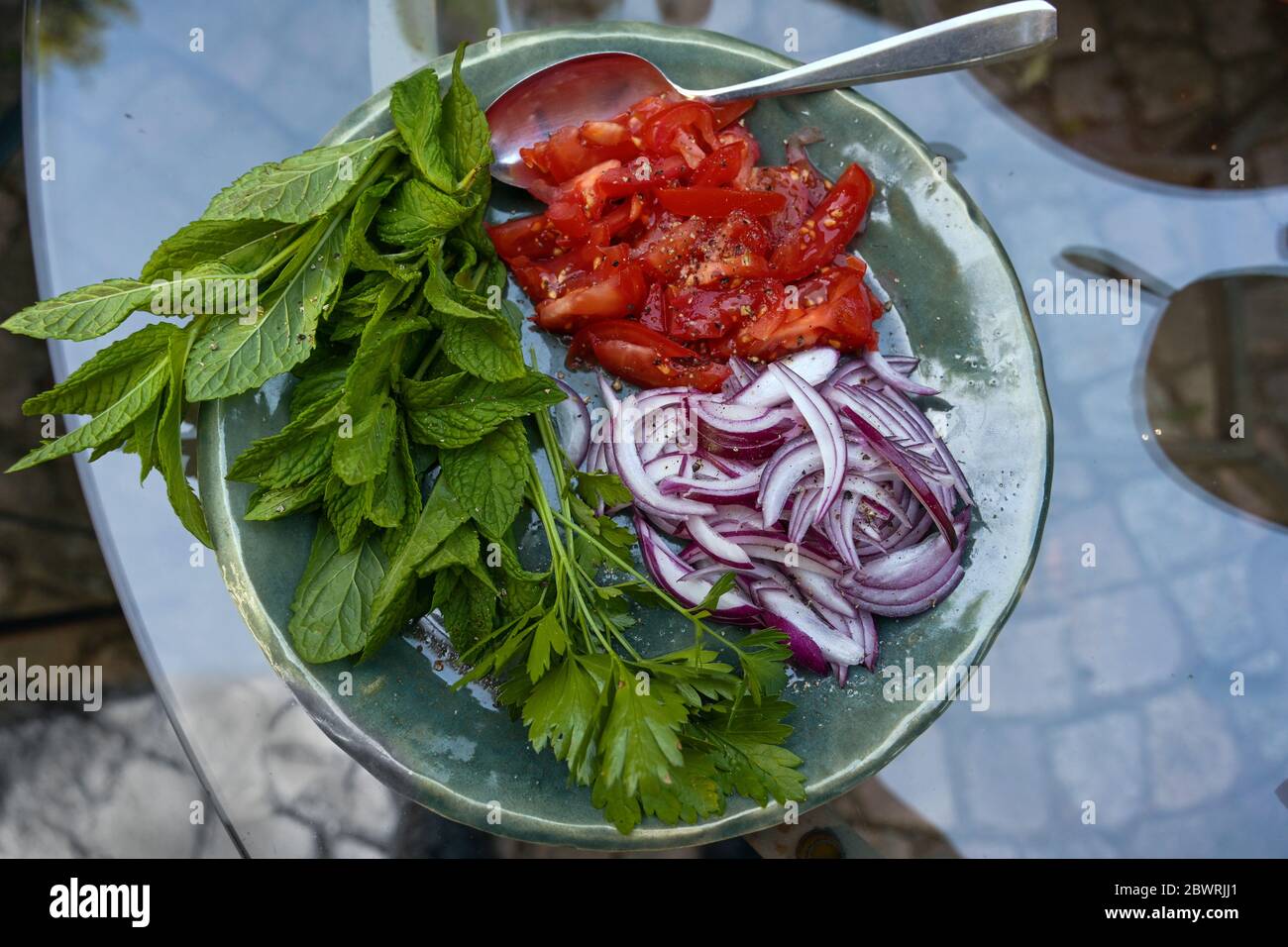 Raw ingredients for a fresh salad or wrap stuffing with red onions, tomatoes and herbs in a rustic bowl on a glass garden table, high angle view from Stock Photo