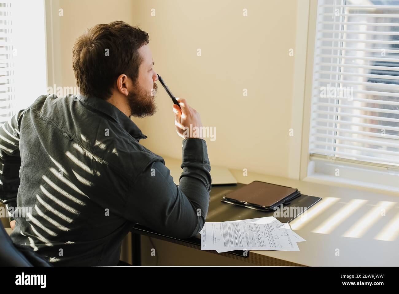 Thinking bearded businessman sitting at office with documents, tablet on table. Stock Photo