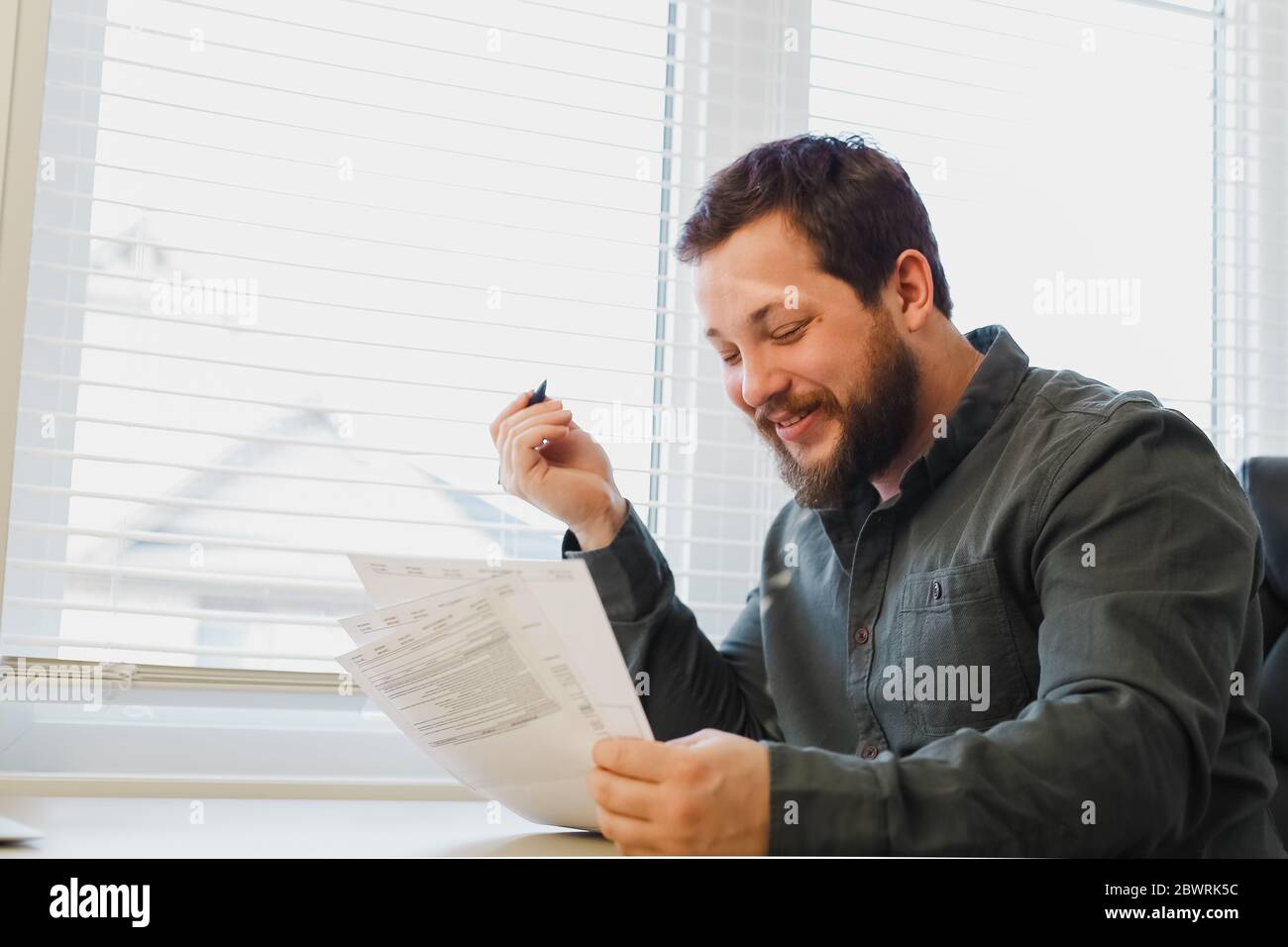 Successful financier reading and filling documents at office near window. Stock Photo